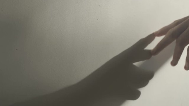 Hand passes over a white wall with hard shadows from window