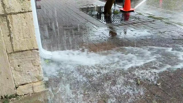 Rainfall rushes through rain gutter onto city pavement during heavy downpour