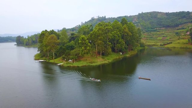 Aerial over a motorboat longboat canoe traveling on a lake in a lush part of Uganda, Africa.