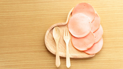 Ham stacked on a heart shape wooden cutting board placed on a Wooden table. Homemade sandwich breakfast preparing. Cooking ingredient. Food background concept with copy space.