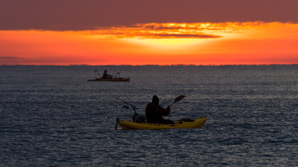 Two anglers paddle kayaks early in the morning before sunrise to go fishing in the Mediterranean.