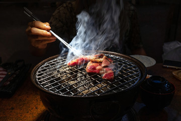 Female hand holding chopsticks picking up charcoal grilled beef