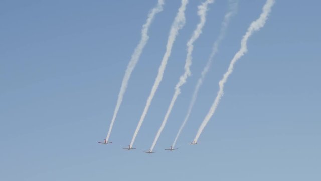 Five vintage war planes fly in formation leaving contrails behind in the blue sky