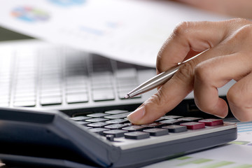close up soft focus businesswoman hand holding pen and press button calculator at office desk with statistics paperwork statement document. Business concept. Copy space for advertisers.