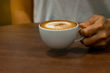 Closeup woman hands holding cup of hot coffee latte cappuccino on wooden background. Food and Drink concept. Using space for advertisers or background.