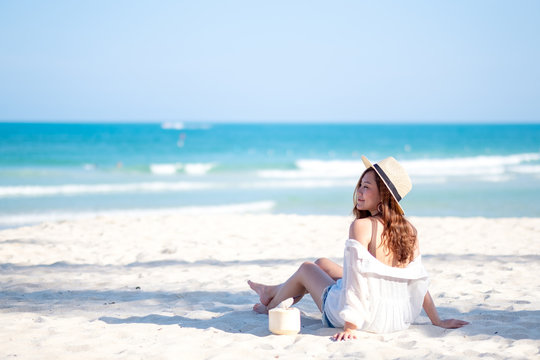 Portrait image of a beautiful asian woman enjoy sitting and drinking coconut juice on the beach