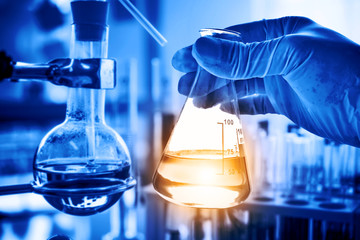 Flask in scientist hand with lab glassware background in laboratory. Science or chemical research and development concept.