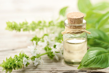 basil essential oil in the glass bottle, with fresh flowers, on the wooden board