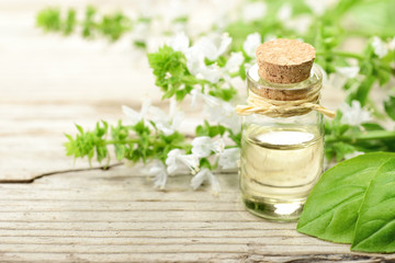 Basil essential oil in the glass bottle, with fresh basil flowers, on the wooden board