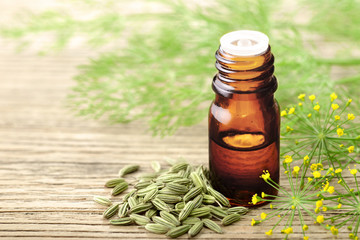 fennel essential oil in the glass bottle, with seeds and flowers, on the wooden board