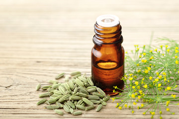 fennel essential oil in the glass bottle, with seeds and flowers, on the wooden board