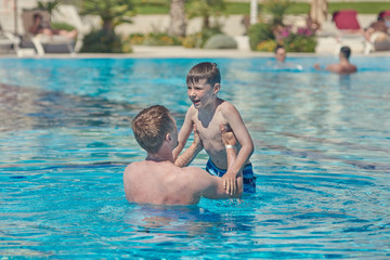 Handsome European man and his son are having fun in the swimming pool. They are enjoying their summer holidays.