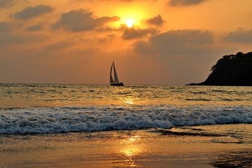 Agonda Beach by Sunset with sailboat on the Ocean and cliff, Goa, India