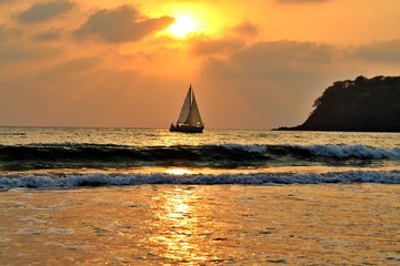 Agonda Beach by Sunset with sailboat on the Ocean and cliff, Goa, India