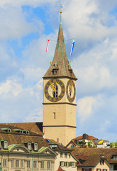 Tower of the St. Peter Church in the Swiss city of Zurich above buildings of the historic part of the city against cloudy sky.