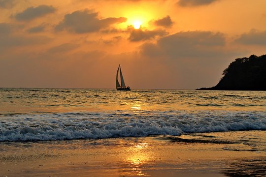 Agonda Beach by Sunset with sailboat on the Ocean and cliff, Goa, India