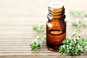 Thyme essential oil in the glass bottle, with thyme flowers.