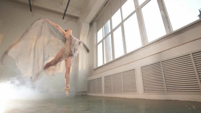Adorable dark-haired ballet dancer in grey fishnet fabric costume with cape dancing in expressive manner over white background, slow motion