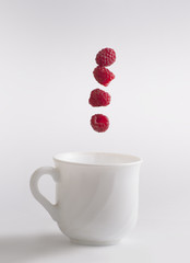 Cup in which raspberry falls, on a gray isolated background