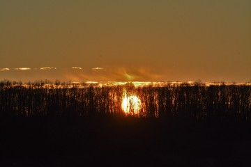 the sunset between the trees on the hill