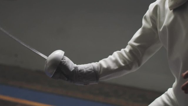 Silhouette of a male fencers epee mask and foil as they strike in a dark and dusty gym