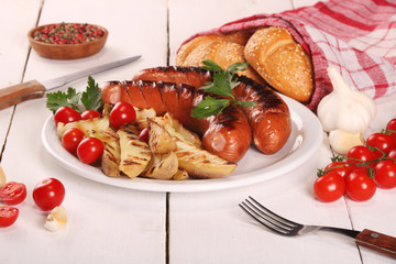 Grilled sausages with vegetables, spices and bread in white plate on white wooden table
