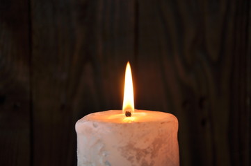 Fototapeta na wymiar a large candle burns in the darkness on a wooden texture background