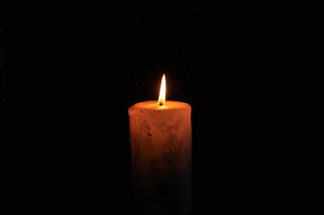 a large candle burns in the dark. On a black background