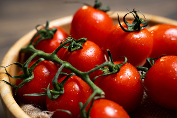 Fresh cherry tomatoes in a plate on a dark wood background.