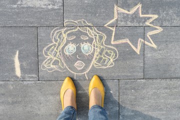 Abstract pop art woman face, picture written on gray sidewalk in crayons, with women legs in yellow...