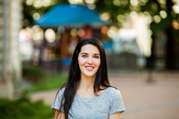 Fototapeta premium Young cute girl in gray shirt with long brunette hair smiling in the street. Close up portrait