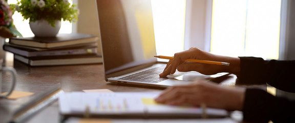 Young businesswoman is sitting at table, working on laptop with graphs, charts on paperwork