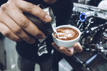 Barista's hand pouring milk to make latte art on cappuccino coffee