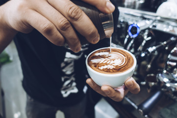 Fototapeta na wymiar Barista's hand pouring milk to make latte art on cappuccino coffee