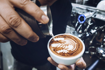 Fototapeta na wymiar Barista's hand pouring milk to make latte art on cappuccino coffee
