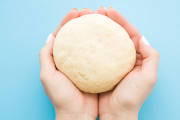 Fresh raw dough in woman's hands. Ready for baking. Closeup. Point of view shot. Light pastel blue table. 