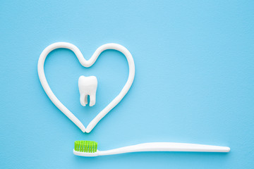 Toothbrush with green bristles on pastel blue background. Heart shape created from paste. White...