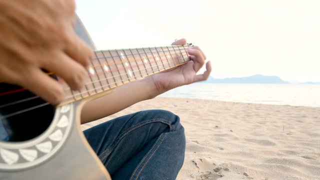 4K. close up of a man playing acoustic guitar at the beach during sunset time, feeling relax
