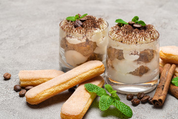 Classic tiramisu dessert in a glass and savoiardi cookies on concrete background
