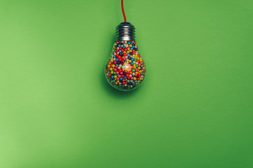 Lightbulb filled with multi colored ball on a green background behind. Best idea concept.