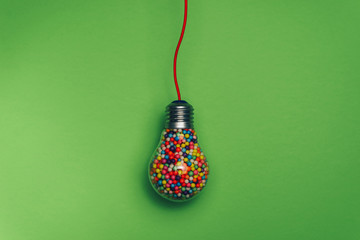 Lightbulb filled with multi colored ball on a green background behind. Best idea concept.