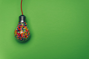 Lightbulb filled with multi colored ball on a green background behind. Best idea concept.