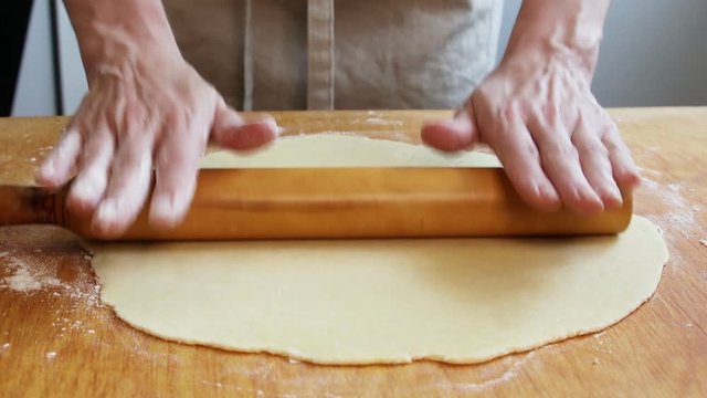 Female hands rolling dough with rolling pin for pastry on wooden table