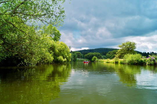 Travelers with paddle and kayak on a small river,  river named lahn in Germany with trees on riversides, landscape image, paddling in a kayak