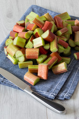 Pile of sliced rhubarb and knife on a blue tea towel with a grey wood background