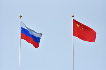 Russian and Chinese flag, symbol of friendship. China and Russia flag waving in the wind against white cloudy blue sky together. Diplomacy concept, international relations.
