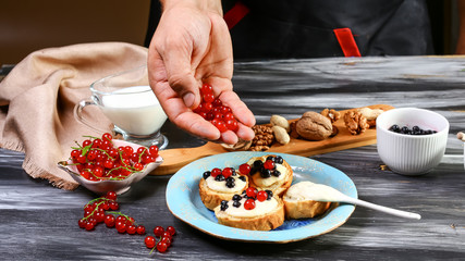Cooking Toast crostini with fresh berries blueberry, red currant and honey, Ricotta cheese. Food recipe on wooden background