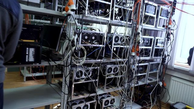 Cryptocurrency equipment, man in sports suit standing in front of the mining money electronic farm, finance concept. Stock footage. Bitcoin farm with working computer equipment.