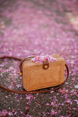 A woven bag stands on the ground in a flowered garden. Sakura.