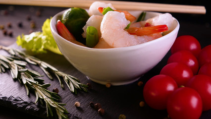 A chef in white gloves prepared a sea dish (salad), decorates with shrimps rubbing parmesan cheese and squeezing lemon juice on top using Chinese sticks, then tasting. Background of cherry tomatoes.